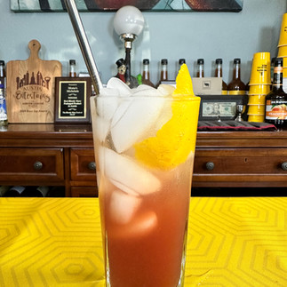 Tall fruity cocktail with citrus garnish on yellow bar surface, refreshing Texas cocktail recipe