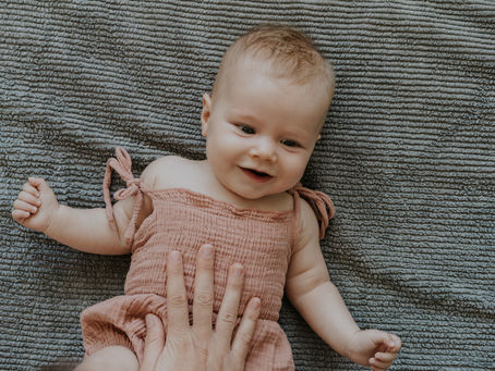 baby laying on a grey towel smiling at pracitioner
