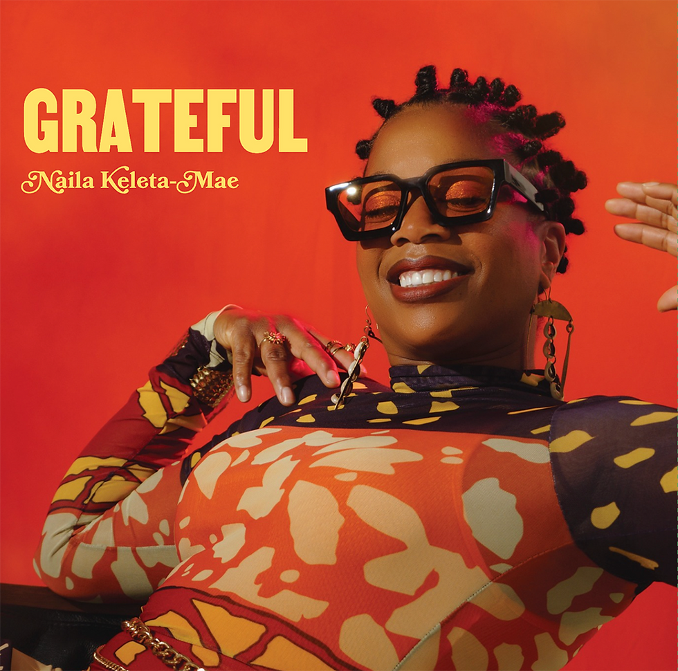 A photo of Naila Keleta-Mae at a photoshoot for her 'Grateful' Album. The background is a coral red with the album title.