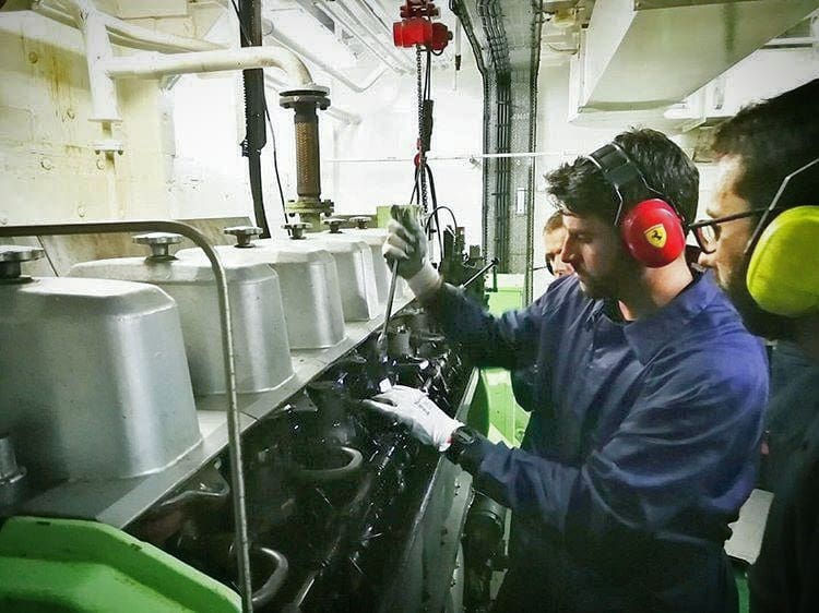 Three men in industrial gear and ear protection work on a large gray machine in a brightly lit room, focused and attentive in Miami, FL.
