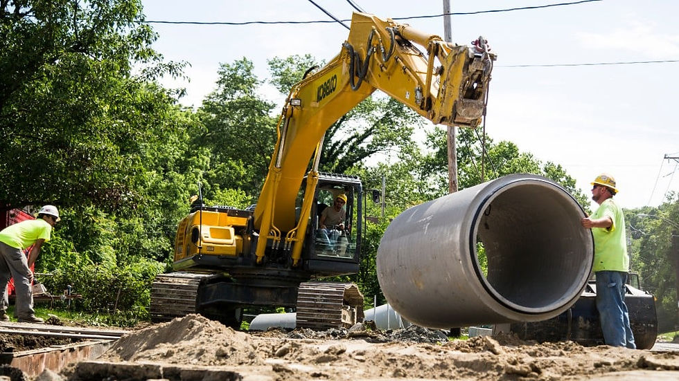Workers in safety gear and a yellow excavator lift a large concrete pipe in a wooded outdoor setting under a clear sky in Fort Lauderdale, FL.