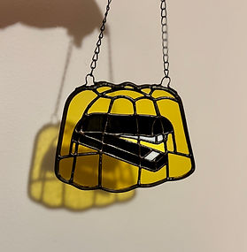 Stained glass stapler encased in yellow gelatin, hanging by chains against a light background.