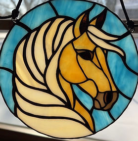 Custom stained glass horse portrait of Halia, showing a golden horse in profile with a flowing mane on a blue background.