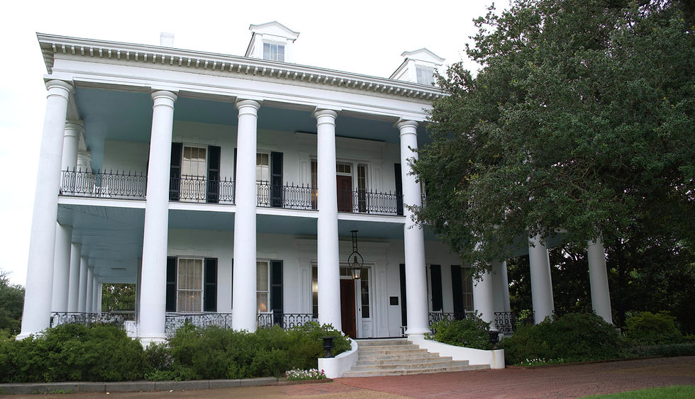 Dunlieth Historic Inn - White building with tall columns, black railings, and symmetrical windows. Surrounded by green bushes and a large tree. Classic Southern architecture.