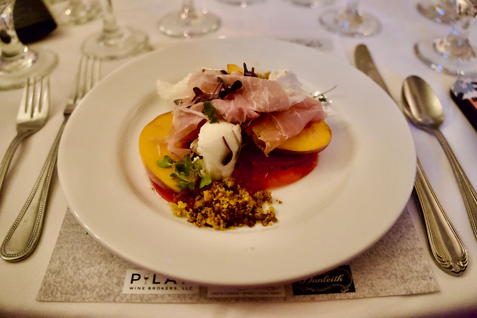 Gourmet plate with prosciutto, peach, greens, and cheese on a white table setting.  Elegant ambiance.