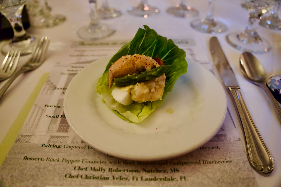 Lettuce wrap with shrimp, egg, and asparagus on a white plate. Set on a table with a menu and glassware in the background.