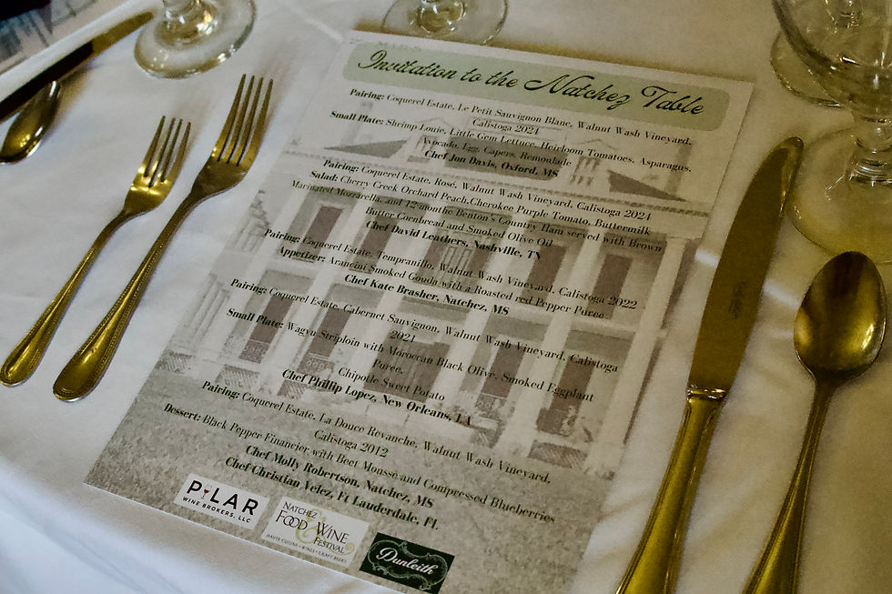 Menu titled "Invitation to the Natchez Table" on a white tablecloth with silverware. Includes pairings and chef names in elegant script.