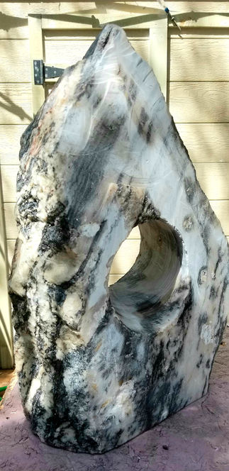 Stone sculpture with a hole, weathered and textured, outdoors on a surface.