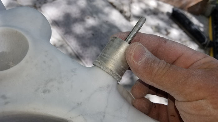 Hand holding a metal burr, working on a white and gray stone surface.