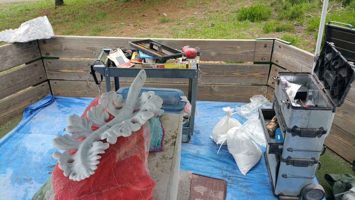 Sculpture in progress on a blue tarp with tools and a wooden background.