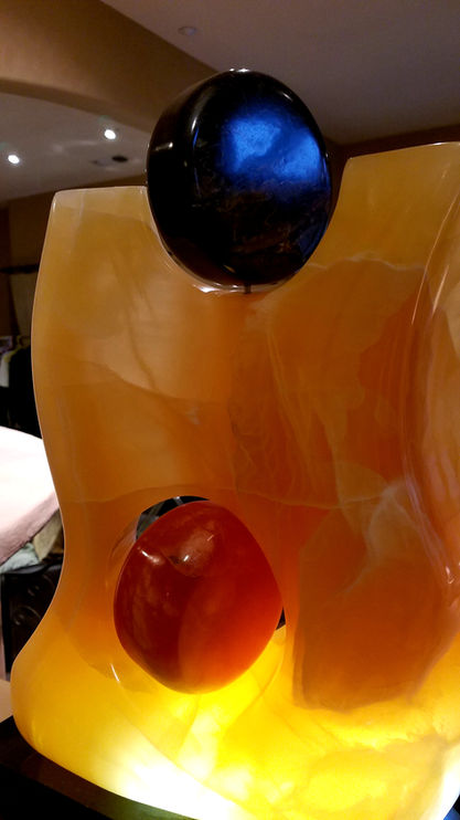 18" T x 6" L x 14" W
Abstract carving of translucent orange calcite encircling a red/orange disc of Utah alabaster. The carving supports another disc of stone with a purple hue of unknown origin. Both discs turn and the Calcite is illuminated with LED lights.