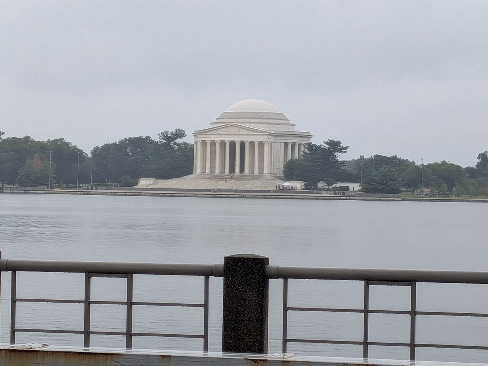 Misty view of the Jefferson Memorial across the water, framed by a railing in the foreground and trees under a gray sky.