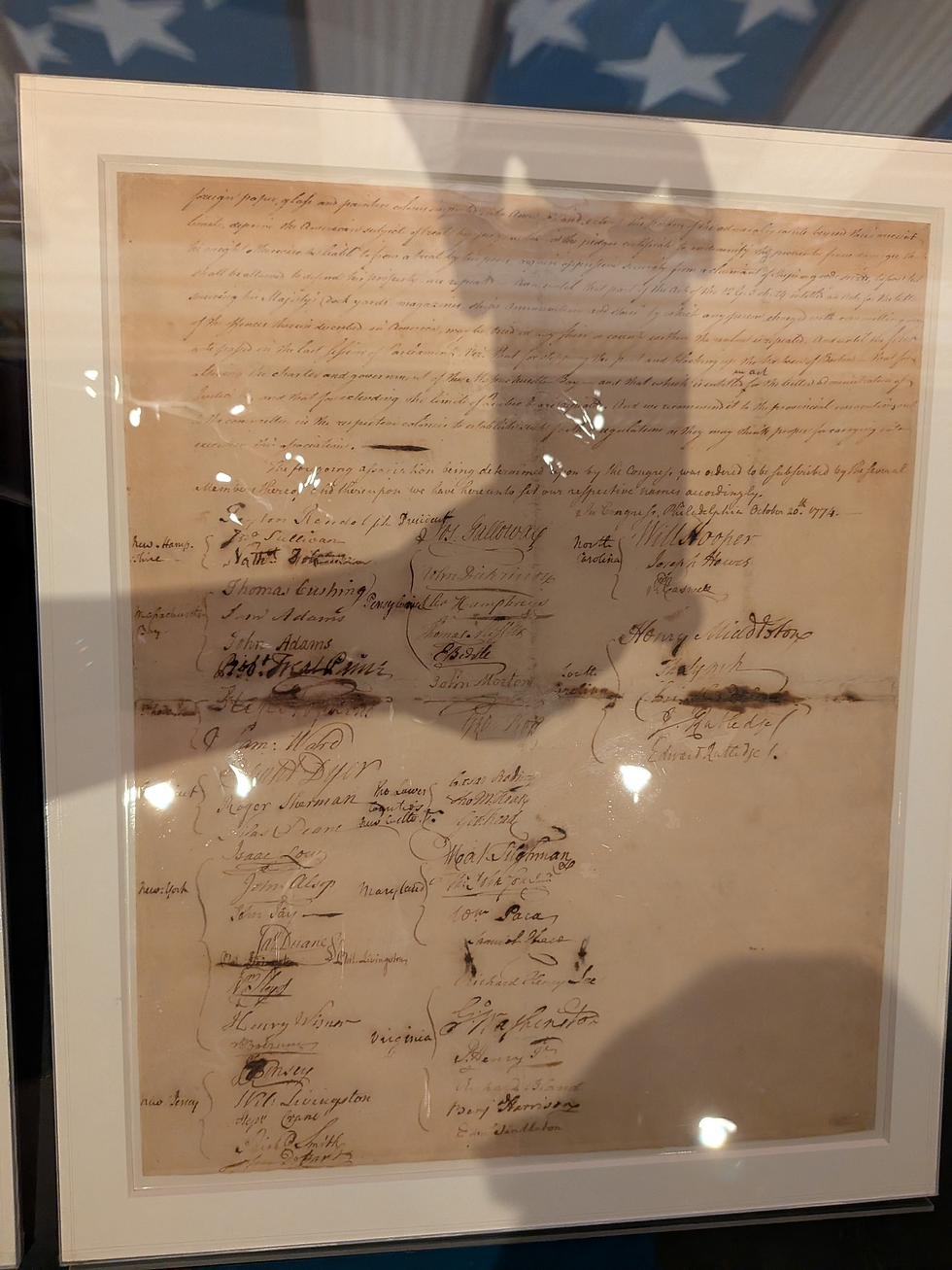 Framed aged handwritten historical document with many signatures and state names, displayed under glass with bright reflections