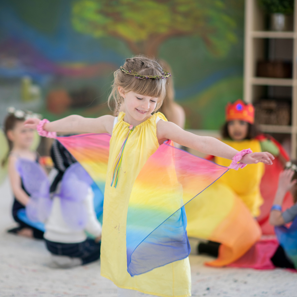 A joyful child wearing a yellow dress and a crown made of flowers, dancing with a colorful rainbow cloth in a classroom setting. The scene reflects Waldorf-inspired play, encouraging creativity, imagination, and connection to nature. Keywords: Waldorf play, imagination, creativity, nature-based learning.