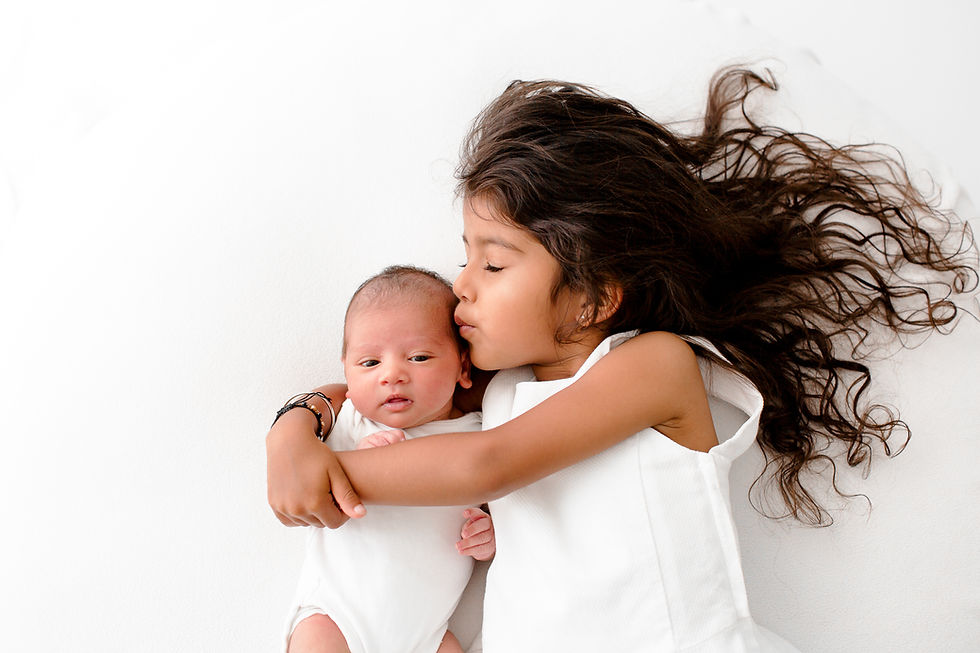 big sister kissing newborn baby whilst laying down and hugging her