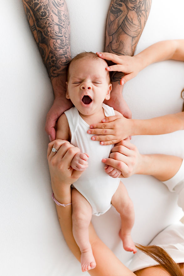 yawning newborn baby with his family's hands holding him