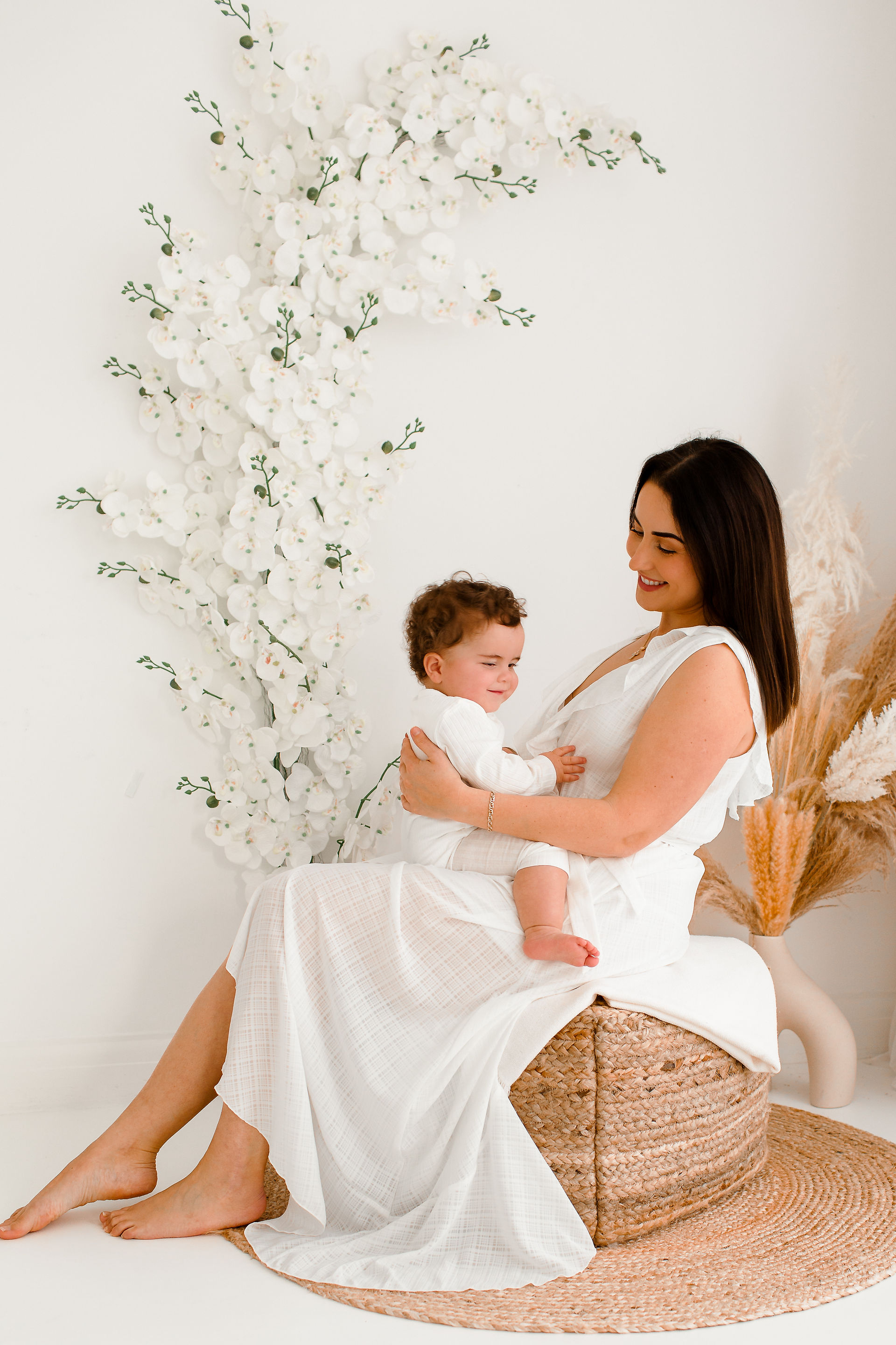 mother in a white dress sitting with her baby son on her lap smiling