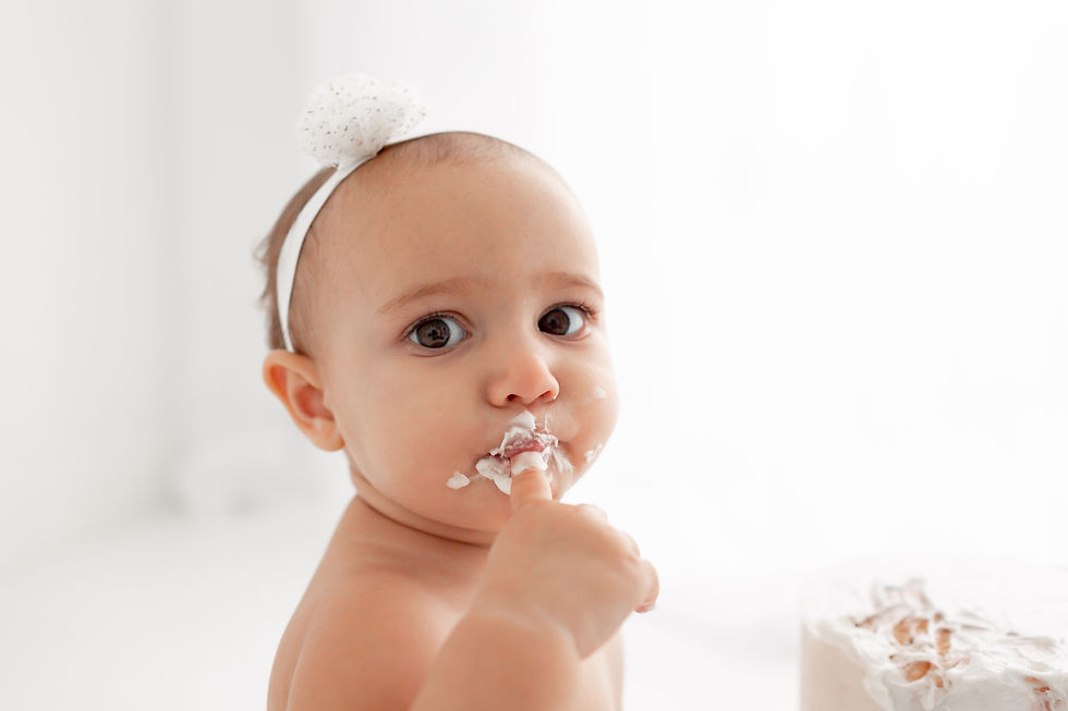 baby licking buttercream off her finger looking at the camera