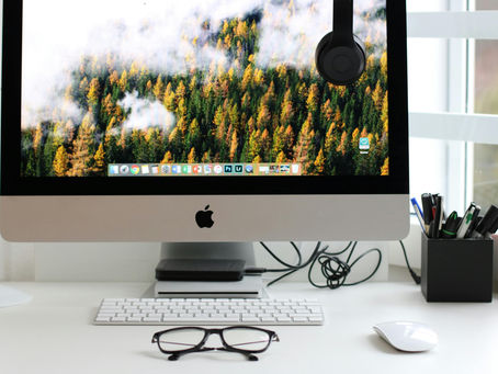 Image of an Apple iMac on desk with keyboard, mouse, glasses, and pencil organizer.