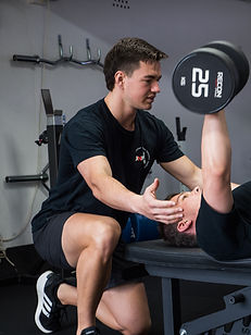 Personal trainer , Jeremy Nissen, helping client with flat dumbbell bench press
