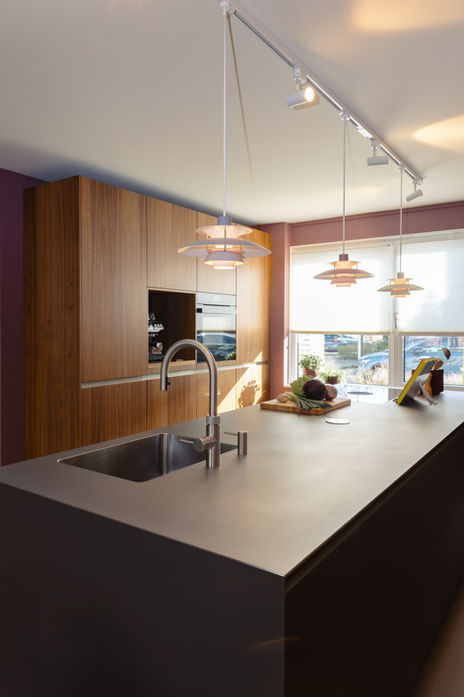 Keukeneiland met RVS blad en mat glazen frontjes in paars. Wandkast van notenhout.