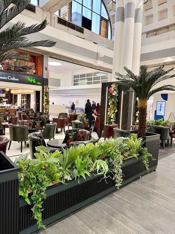 Bespoke artificial greenery planters and statement palm trees creating a lush botanical interior for a modern café and commercial hospitality space by SDesign Floral.