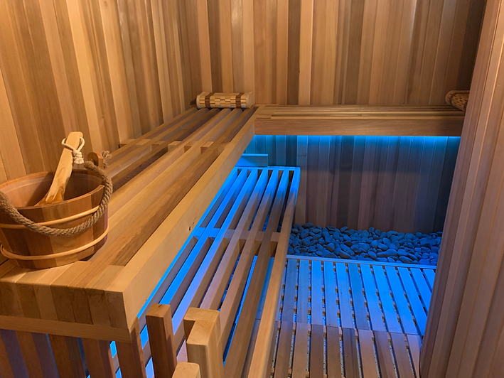 Custom cedar home sauna with integrated benches, under-lighting, and stone detail by Peri's Line