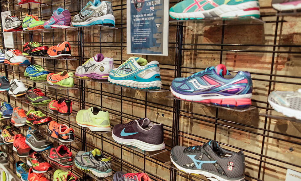 Colourful running shoes displayed on metal racks against a brick wall. A sign on the wall notes "May 8, 2014." Bright and organized setting.
