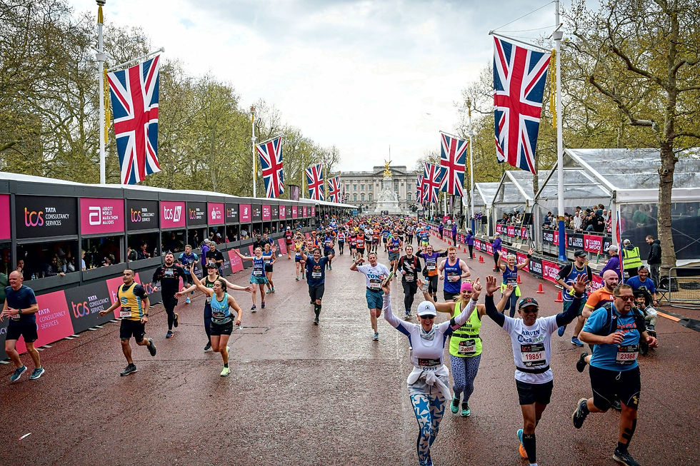 Runners joyfully finishing the London marathon on a road lined with UK flags. Cheerful crowds watch from the side. Overcast sky, festive mood.