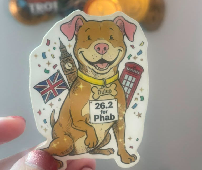 Smiling dog sticker named Dulce with 26.2 for Phab bib, surrounded by UK flag, Big Ben and red phone box confetti.