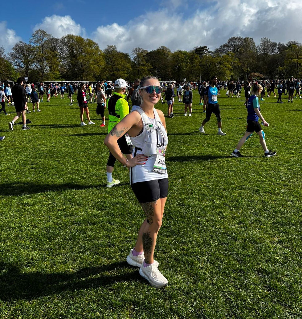 Olivia Harman in sunglasses at the start of the Brighton Marathon, surrounded by runners. Trees and cloudy sky in the background, sunny day in Preston Park.
