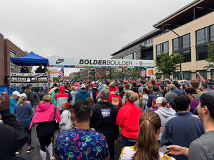 Crowd of runners gathers at the BOLDERBOULDER старт line under a city arch on a gray day, with flags, stage, and cheering officials. By Jsdratm - Own work, CC0,