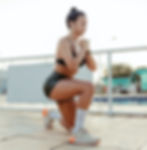 Woman in black sportswear doing a lunge on a sunlit outdoor deck, focused and determined.