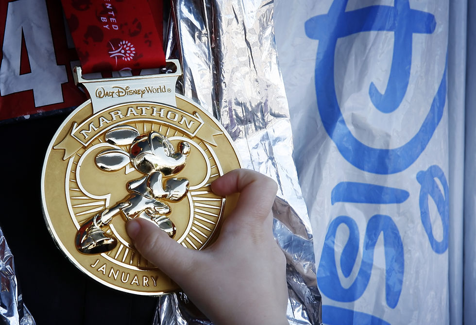 Volunteer's hand holding a gold marathon medal featuring a mouse, with Disney World text. Silver foil and blue-patterned background create a celebratory mood.