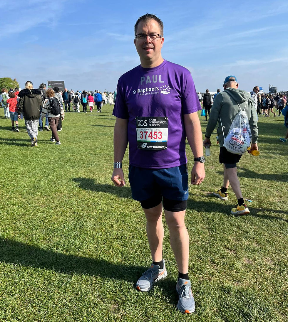 Man in a purple shirt with "St. Raphael's" text stands on a grassy field with a marathon bib numbered 37453, surrounded by people.