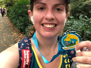 Sophie Badman takes a selfie on a leafy park path, wearing a cap and medal, holding a Battersea medal and water bottle.