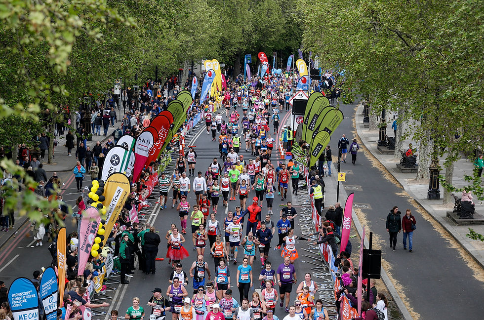 Crowd of London marathon runners on Victoria Embankment, surrounded by colourful banners and cheering spectators. Energetic atmosphere.