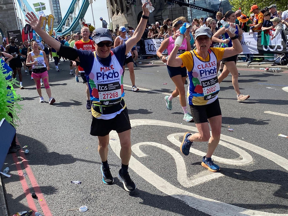 Phab charity runners in colourful gear joyfully raise arms during the London marathon. Crowds cheer near a bridge in a sunny urban setting. Bibs visible.