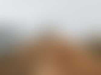 Woman stands with arms raised on a golden mountain ridge above a cloudy valley and river, feeling triumphant.