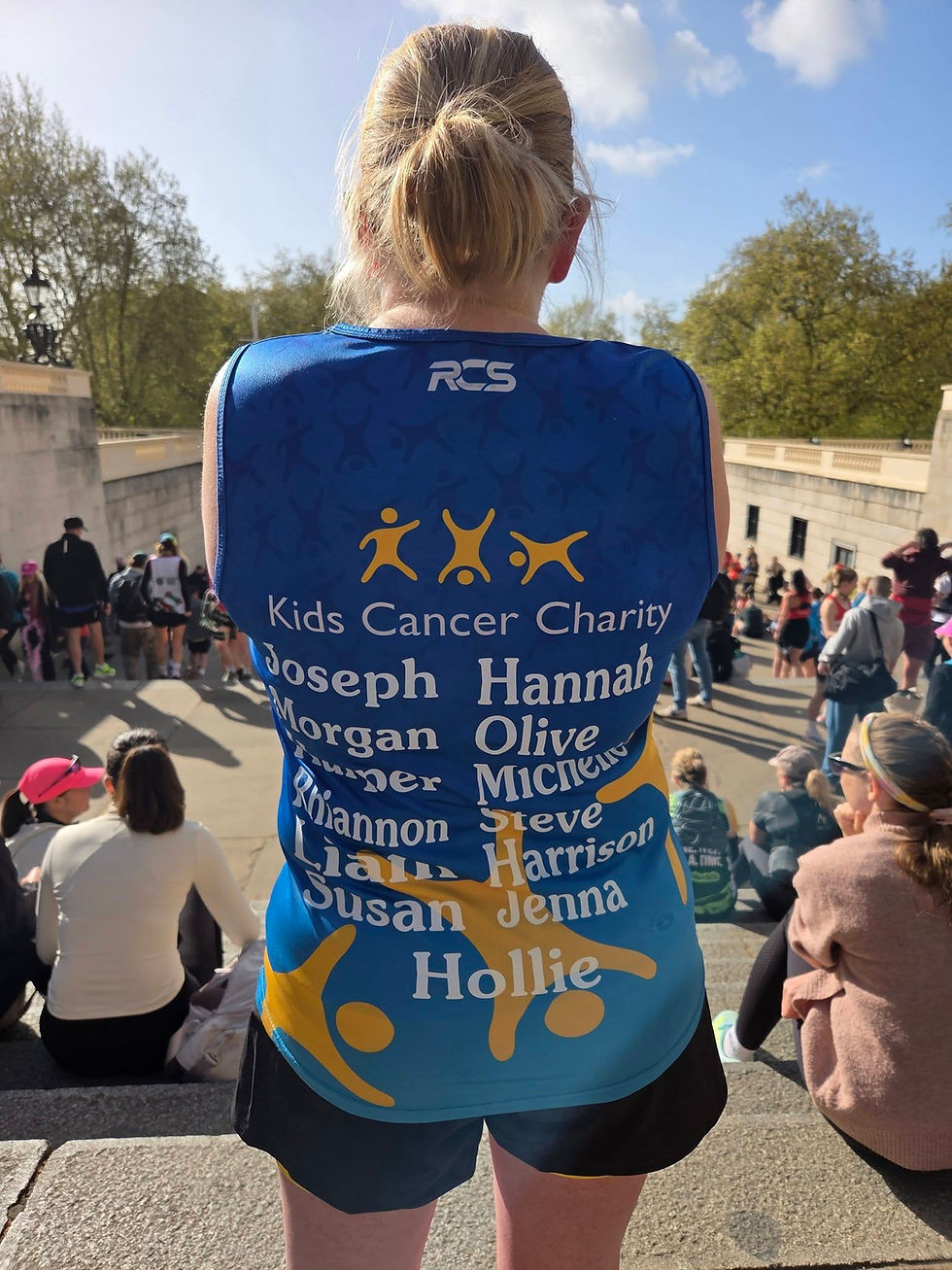 Alice Sullivan in blue Kids Cancer Charity vest stands among seated spectators outdoors under a sunny sky, with names printed on back.