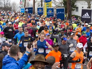 Crowd of runners in colourful attire during the Boston Marathon, surrounded by spectators. Blue Adidas signs and trees in the background. Energetic mood.