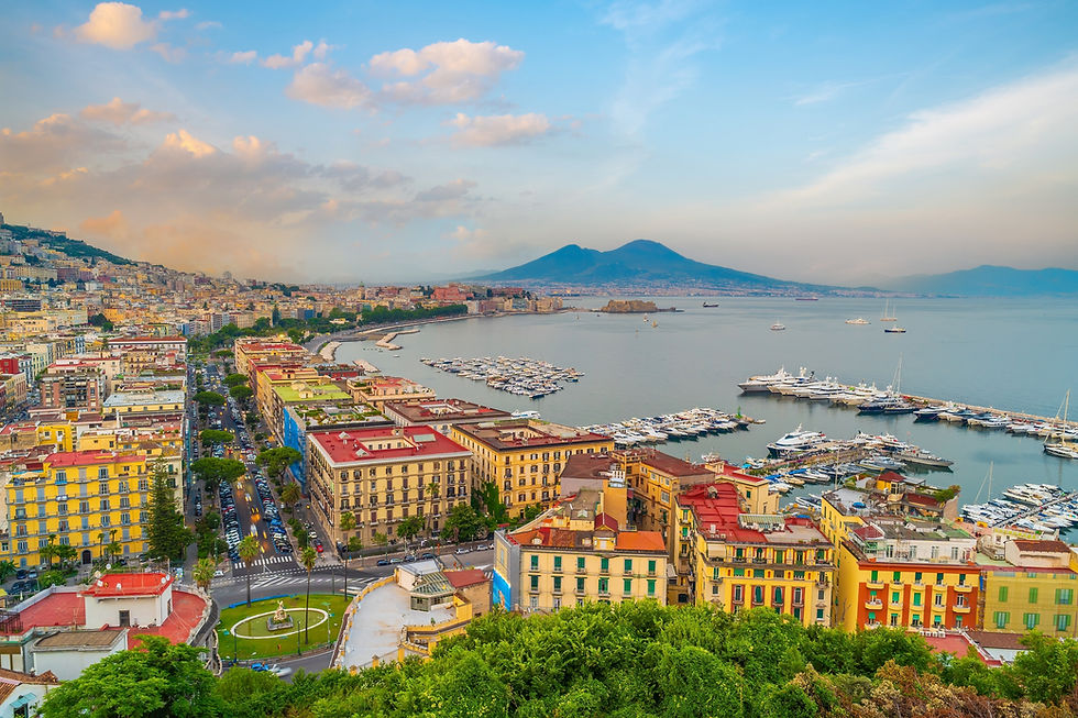Naples with Vesuvius in the background, with yachts in a calm bay under a soft blue sky.