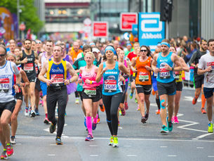 Runners in bright outfits compete in a lively city marathon. Bib numbers and brand logos visible, with cheering crowds in the background.