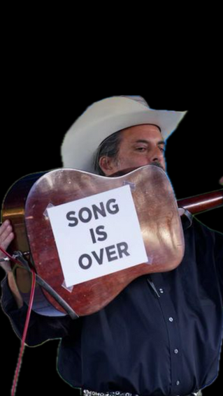 The King Teen holding up his guitar to show the back of it to the audience. A sign taped on it says SONG IS OVER.