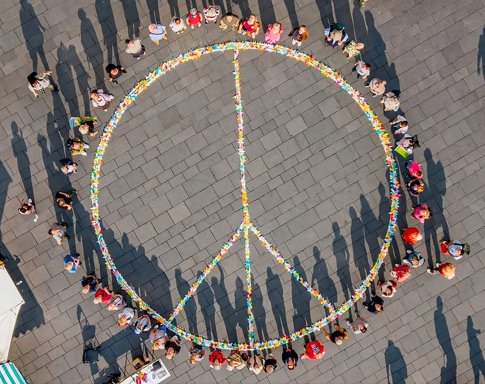 Menschen bilden auf dem Marktplatz ein Peace-Zeichen aus bunten Blumen als Symbol für Frieden und Gemeinschaft.