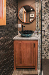 A round mirror in wood frame above the art glass vessel sink vanity with water pump faucet
