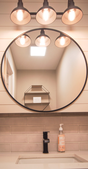 Vintage look wall lighting above round mirror in guest bath of Roger's Family Home by Barrett Home Renovations