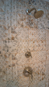 Brushed nickel shower head, faucet, and temperature handle on wall of artisan patterned square tiles
