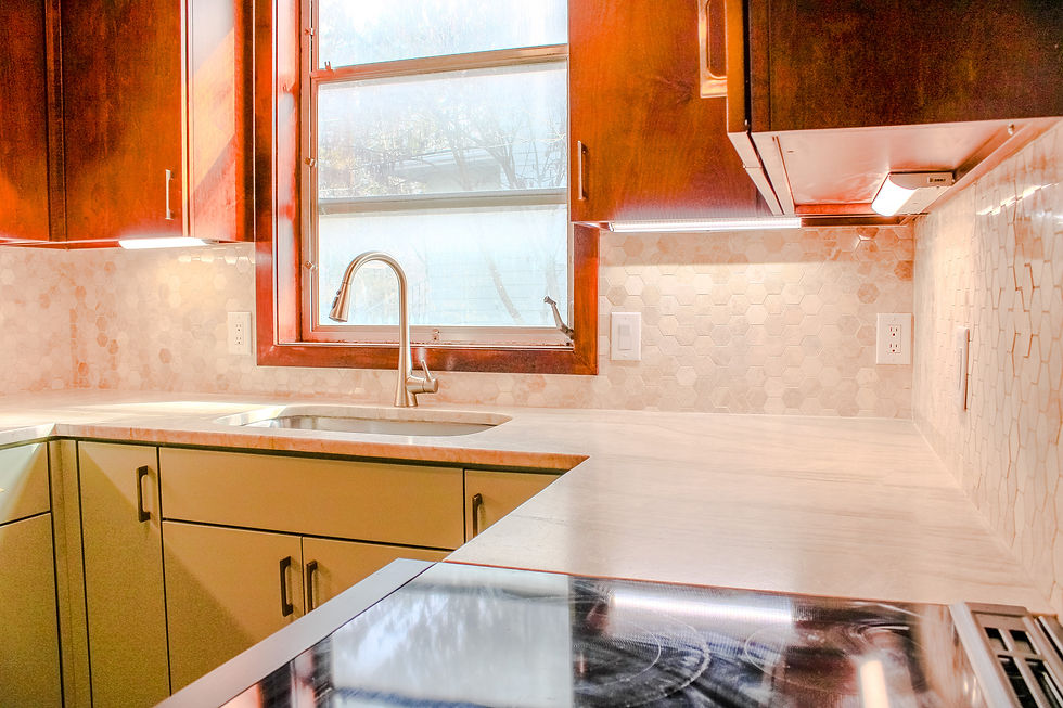 countertop view of kitchen sink with bottom of warm wood cabinets showing, mosaic beige backsplash, and green bottom cabinets