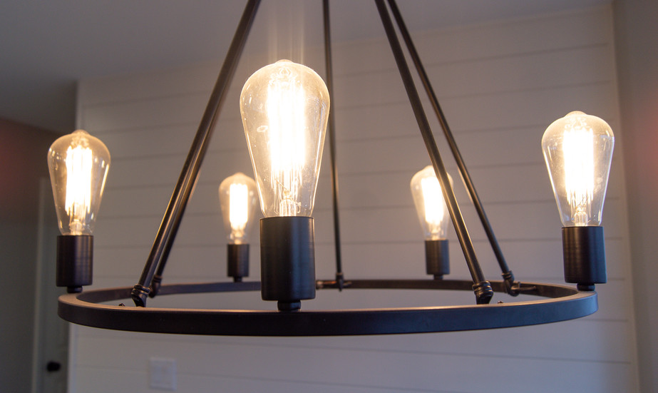 Open wheel wrought iron chandelier with vintage-look Edison lights hung by Shiplap wall in dining area